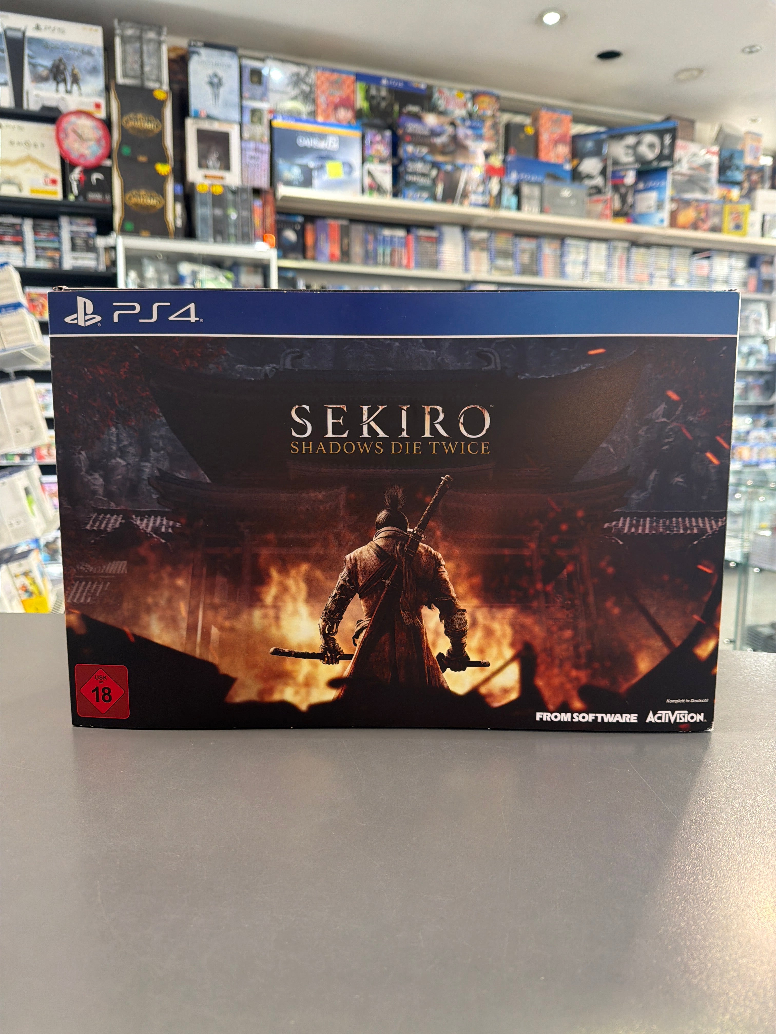 „Produktbild der Collector’s Edition von Sekiro Shadows Die Twice für PlayStation 4 mit Figur des einarmigen Shinobi, Steelbook-Hülle, Artbook, gedruckter Karte, digitalem Soundtrack und dekorativen Münzen, arrangiert in einer Sammlerbox“